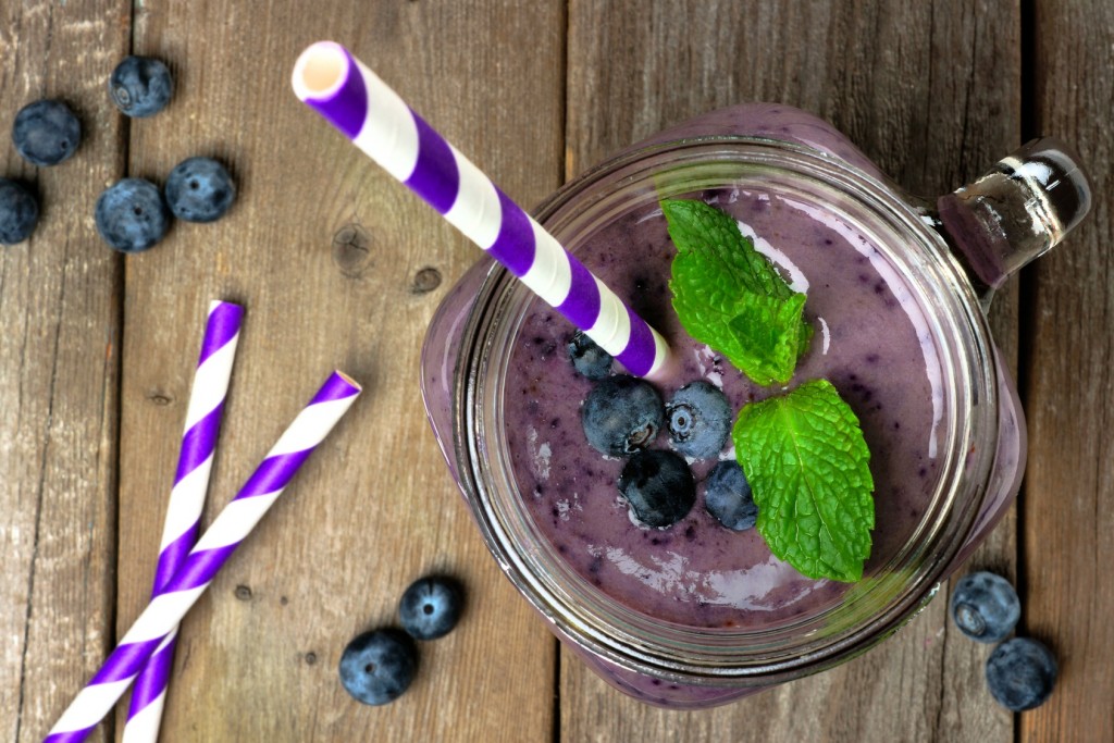 Blueberry smoothie with mint in mason jar mug with straw. Overhead view on wood.